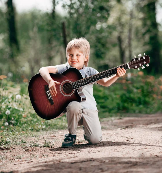Parktaki bulvarda gitarlı küçük çocuk. — Stok fotoğraf