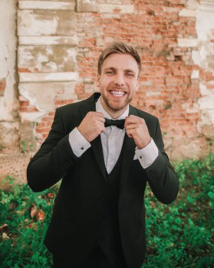 Genç ve mutlu damat eski tuğla duvarın yanında duruyor..