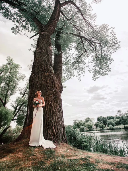Noiva feliz em pé por uma grande árvore velha . — Fotografia de Stock