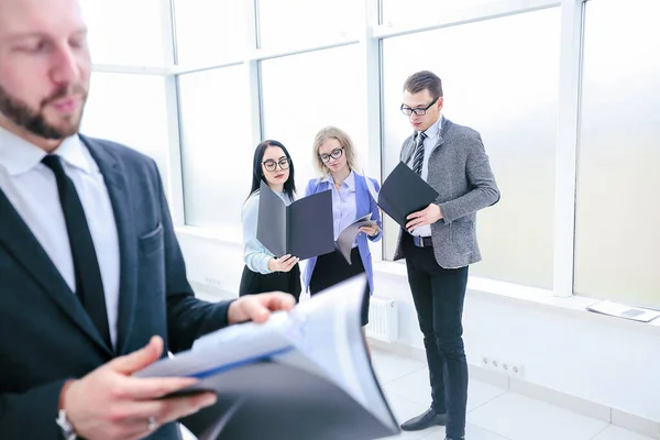 Uomo d'affari ei suoi colleghi che studiano i documenti aziendali in piedi in ufficio . — Foto Stock