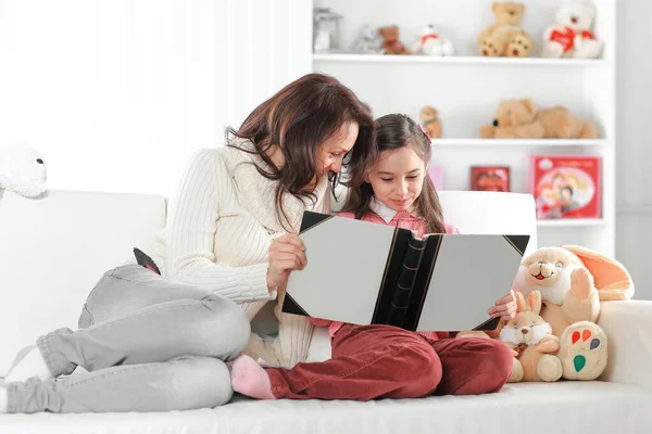 Affascinante madre e figlia leggendo un libro seduto sul divano. Foto con spazio copia — Foto Stock