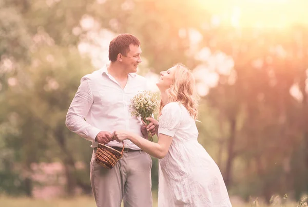 Glückliches Paar - schwangere Frau und ihr Mann in einem Park mit Gänseblümchen — Stockfoto