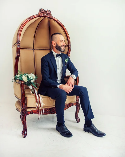 Hombre elegante sentado en una silla y mirando en algún lugar a un lado . — Foto de Stock