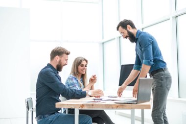 Bir grup iş adamı ofis masasının yanında bir şey tartışıyor.