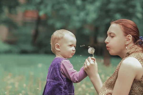 Jeune mère enseigne à sa petite fille à souffler sur un pissenlit — Photo