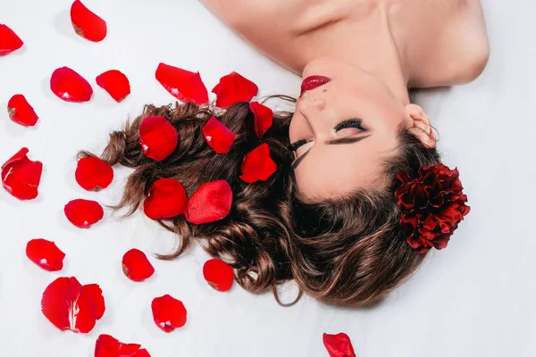 Schöne junge Frau liegt mit Rosenblättern im Bett. — Stockfoto