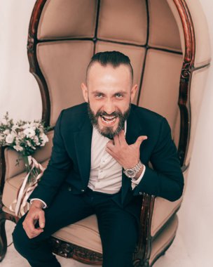 Kapat. Şık bir sandalyede oturan neşeli damat.