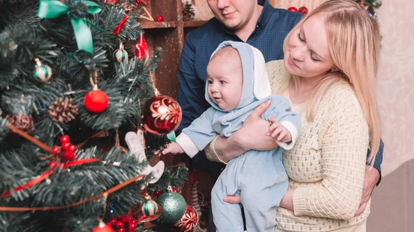 Gelukkige ouders en hun baby staan naast de kerstboom — Stockfoto