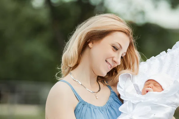Young mom with newborn baby on blurred nature background. — Stock Photo, Image