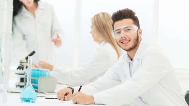 Kapat. Laboratuvardaki masasında oturan genç bilim adamı.