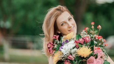 Park 'ın bulanık arka planında bir buket çiçekle güzel bir kadın.