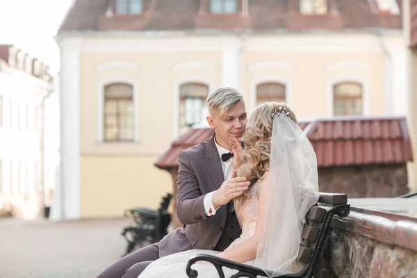 bride and groom sitting on a bench on a city street.