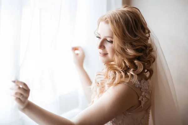 De cerca. mujer joven en vestido de novia de pie cerca de la ventana. — Foto de Stock