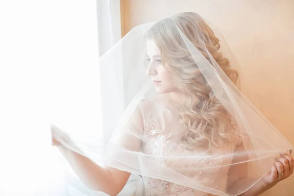 Zárj be! gyönyörű fiatal nő esküvői fátyol néz ki az ablakon. — Stock Fotó