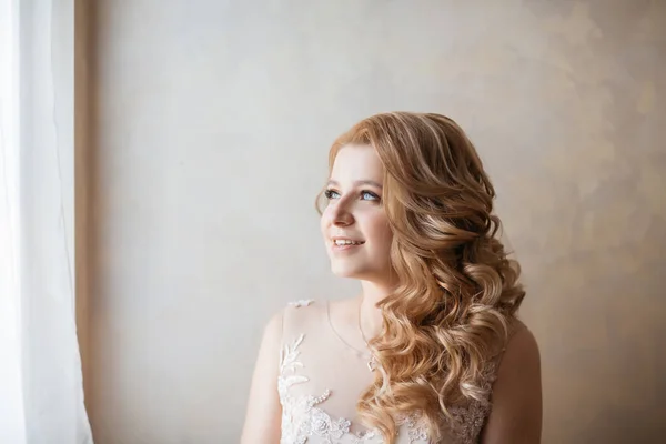 Nahaufnahme. junge Frau im Hochzeitskleid steht am Fenster. — Stockfoto