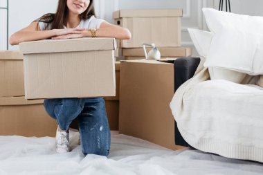 Karton kutulu genç bir kadın yeni bir dairede yerde oturuyor.