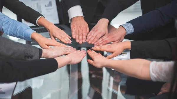 Equipo de negocios que se une a ellos en la palma de su mano sobre el escritorio . — Foto de Stock