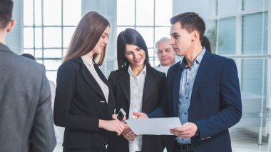 Bir grup genç çalışan iş molası sırasında ofis lobisinde duruyorlar.