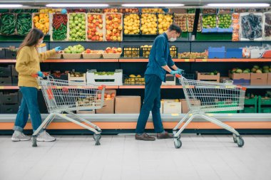 Karantina döneminde süpermarkette alışveriş arabalı bir adam ve bir kadın..