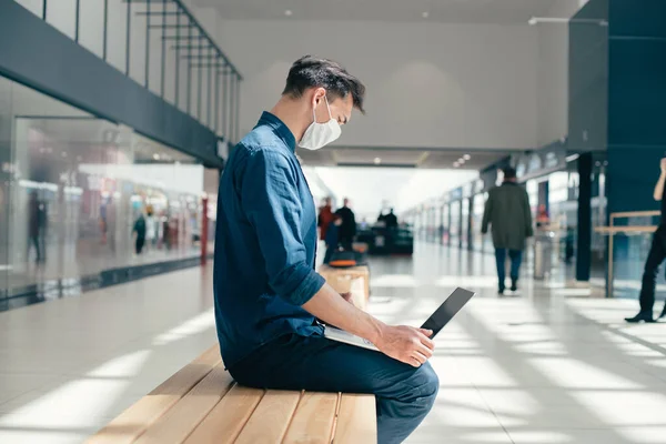 Mann mit Schutzmaske arbeitet in der Nähe eines städtischen Gebäudes an einem Laptop. — Stockfoto