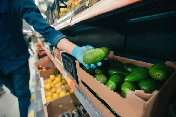 Man in protective gloves takes an avocado from the counter. — Stock Photo, Image