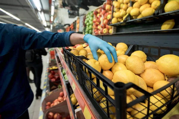 Man in protective gloves takes a lemon from a grocery counter. — Stock Photo, Image