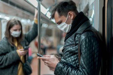 Korumalı maskeli yolcular metro vagonunda duruyorlar..
