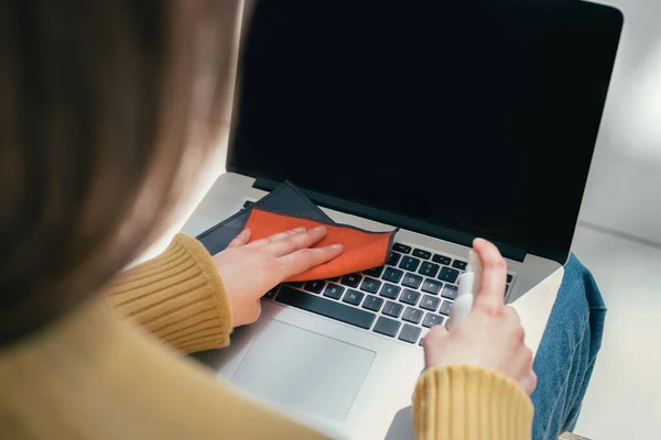 De près. une jeune femme utilise un antiseptique pour nettoyer son ordinateur portable — Photo