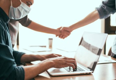 Koruyucu maskeli bir iş adamı ofis bilgisayarında çalışıyor..