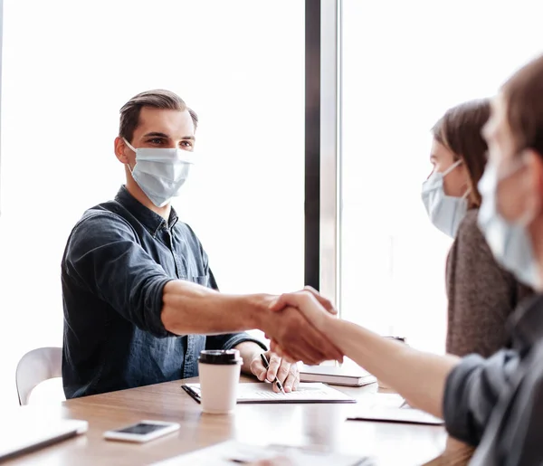 Jonge zakenpartners in beschermende maskers schudden handen met elkaar. — Stockfoto