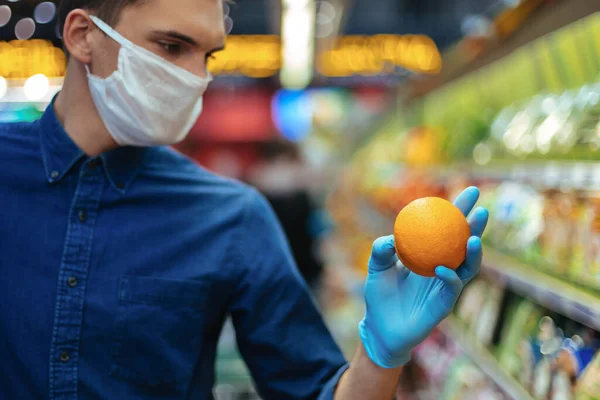 De près. homme dans un masque de protection lors de la sélection des oranges au supermarché. — Photo