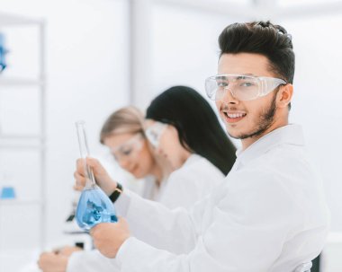 Genç bilim adamı sıvı dolu bir deney şişesi gösteriyor..