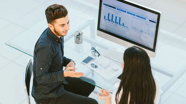 two employees discuss financial data sitting at an office Desk