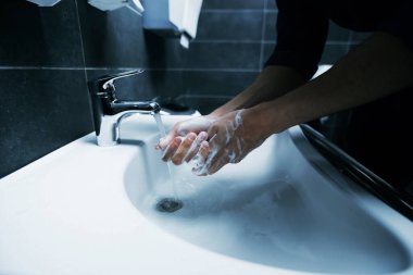 Kapat. Genç bir adam ellerini dezenfektanla yıkıyor.