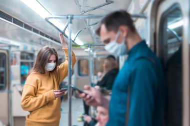 Metro vagonunda duran koruyucu maskeli genç bir kadın..