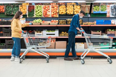 Karantina döneminde süpermarkette alışveriş arabalı bir adam ve bir kadın..