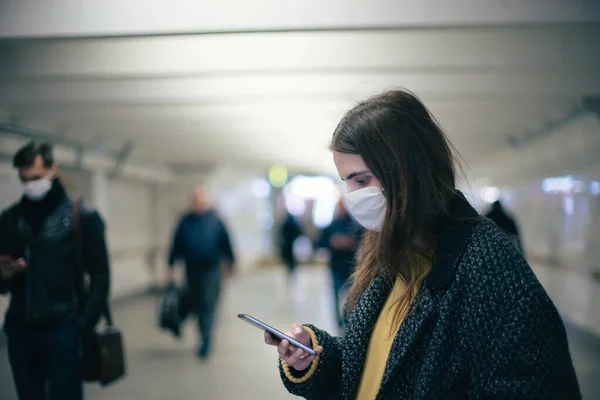 Jovem mulher em uma máscara protetora lendo uma mensagem de texto em uma estação de metro . — Fotografia de Stock