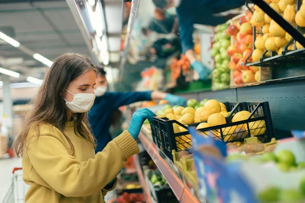 Young woman in a protective mask choosing lemons in a store — Stock Photo, Image