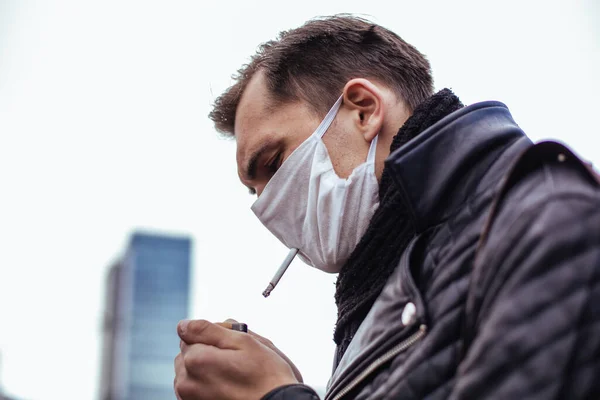 Serieuze man met een beschermend masker rookt op straat. — Stockfoto