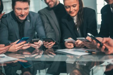 Kapat. Akıllı telefonları olan çalışanlar masada oturuyorlar.