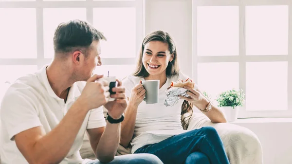 Joven pareja bebe café sentado en el sofá en un nuevo apartamento. — Foto de Stock