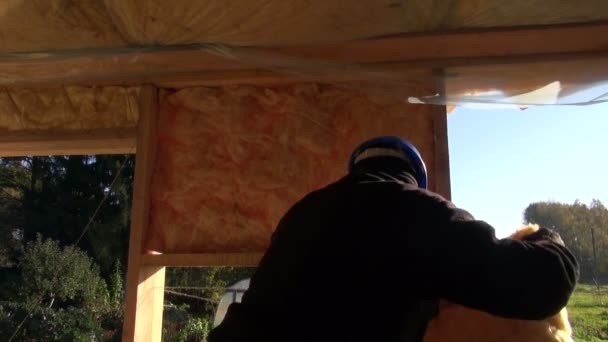Builder with a safety hat insulating house frame — Stock Video