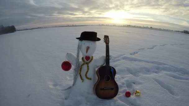 Сніговик на полі з гітарою та різдвяними прикрасами, проміжок часу 4K — стокове відео