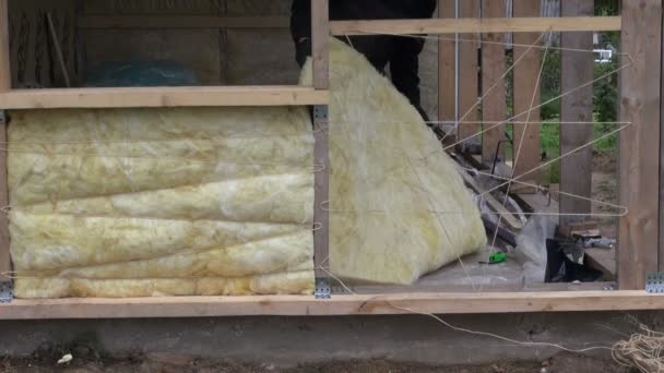 Trabalhador isolante estrutura de casa de madeira com lã de rocha — Vídeo de Stock