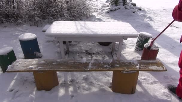 Gärtner reinigt frischen Schnee von Holzmöbeln im Garten — Stockvideo