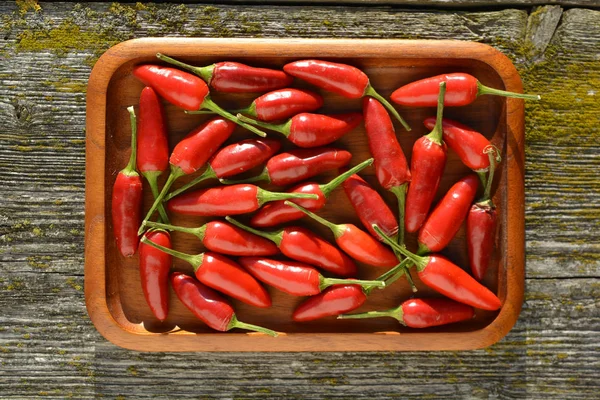 Hot chili peppers in wooden plate on old plank background — Stock Photo, Image