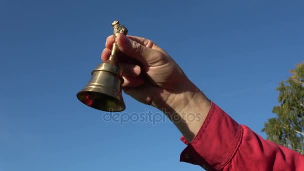 Латунный колокол в руке на фоне неба — стоковое видео