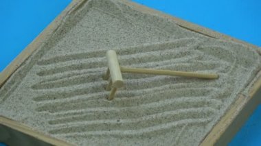 Mavi arka plan üzerinde ahşap komisyon ile dönen küçük kum zen Bahçe kutu