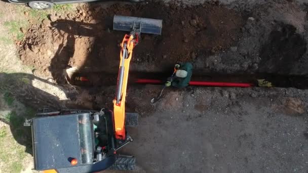 小型挖掘机和工人埋入城市街道壕沟 用管子 — 图库视频影像