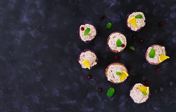 桜クリームとレモンのカップケーキ。クランベリー、ミントの葉。暗い背景の上に食べ物。トップ ビュー — ストック写真